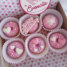 cupcakes with pink frosting and hearts are in a box on a table