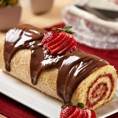 a roll covered in chocolate and strawberries on a plate next to a bowl of strawberries