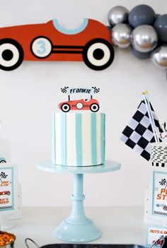 a birthday cake sitting on top of a table next to balloons and streamers in the shape of cars