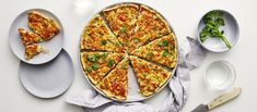 a pizza sitting on top of a white table next to two plates with slices missing