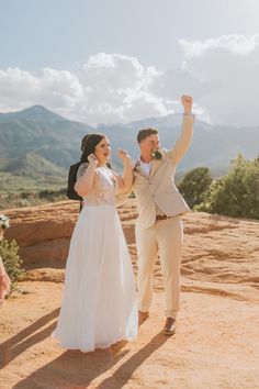 a bride and groom standing on top of a mountain with their arms in the air