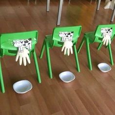 three green chairs with painted hands on them in the middle of a wooden floored room