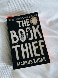 the book thief by markus zusak laying on top of a bed with white sheets