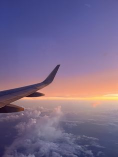 the wing of an airplane as it flies through the sky at sunset or dawn over clouds