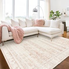 a living room with a large white sectional couch and pink throw pillows on top of it