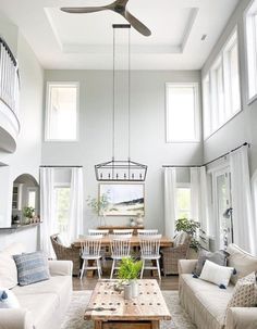 a living room filled with furniture and a ceiling fan above a table in front of two windows