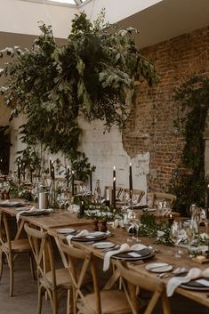 the table is set with place settings and greenery hanging from the brick wall behind it