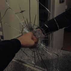 a hand holding a broken glass in front of a door with another hand reaching for it