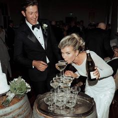 a man and woman standing next to each other with wine glasses in front of them