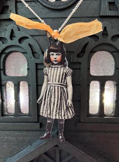 the doll is wearing a yellow ribbon and standing on top of a wooden structure with windows