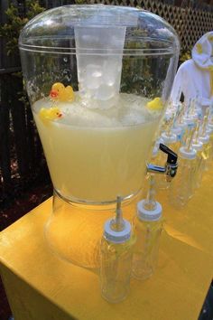 a pitcher filled with liquid sitting on top of a yellow table next to bottles and cups