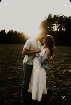 a man and woman standing in the middle of a field at sunset with trees in the background