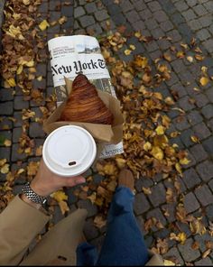 a person holding a coffee cup with a croissant in it's wrapper