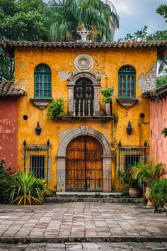 an old yellow building with green shutters and potted plants on the front door