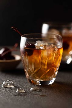 two glasses filled with liquid and ice on top of a table next to an olive