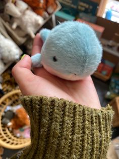 a small blue stuffed animal sitting on top of a person's hand in a store