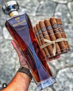 a hand holding a bottle of macallaa and some cigars