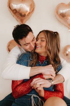 a man and woman hugging each other in front of heart shaped balloons on the wall