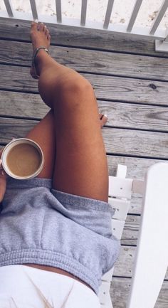 a woman sitting on a white chair with her legs crossed holding a cup of coffee