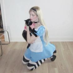 a woman in a blue dress holding a black and white cat while sitting on the floor