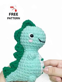 a hand holding a small crocheted toy in the shape of a dinosaur with green hair