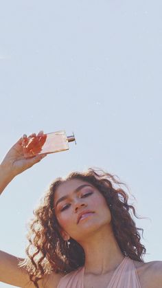 a woman in a pink dress is holding a bottle and looking up at the sky