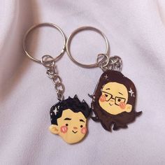 two keychains with cartoon characters on them sitting on a white cloth covered surface