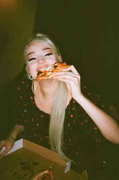 a woman eating a slice of pizza in front of her face and holding it up to her mouth