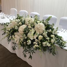 a table with white flowers and greenery is set up for a formal dinner or reception