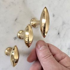 a hand is pointing at three gold knobs on a marble surface with white and black speckles