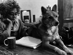 a woman sitting at a table with a dog and book in front of her on the phone