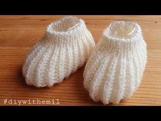 two white knitted baby booties sitting on top of a wooden table