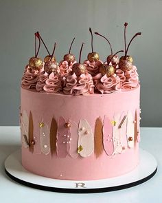 a pink frosted cake with gold decorations on it's sides and flowers on the top