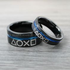 two black and blue wedding rings with the word aoxl on them sitting on a wooden surface