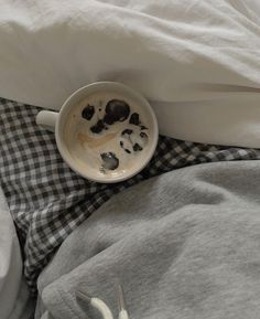 a cup of coffee with chocolate chips in it on a bed next to a pair of utensils