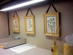 an office cubicle with three paintings hanging on the wall and two vases filled with flowers