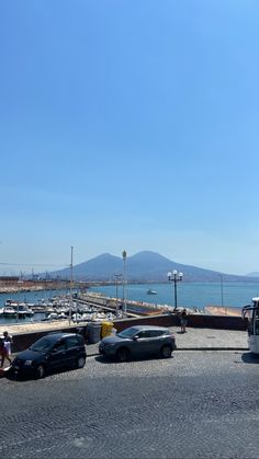 there are cars parked on the side of the road next to the water with mountains in the background