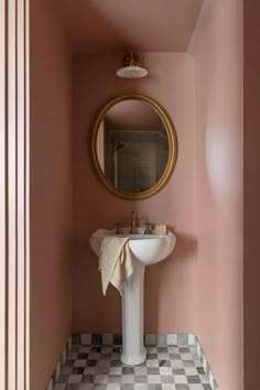 a bathroom with pink walls, checkered floor and a round mirror on the wall