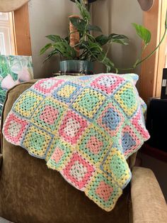 a crocheted blanket sitting on top of a chair next to a potted plant