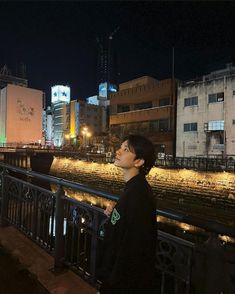 a young man standing on top of a bridge next to a city street at night