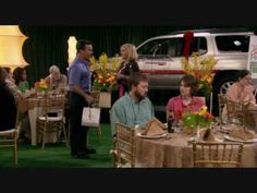 people are sitting at tables in front of a white truck and green carpeted area