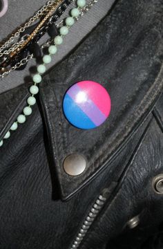 a black leather jacket with a pink and blue button on it