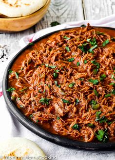 shredded meat in a pan with parsley on top and pita bread next to it