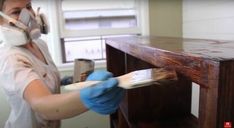 a woman in white shirt and blue gloves painting a wooden table