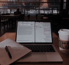 an open laptop computer sitting on top of a wooden table next to a cup of coffee