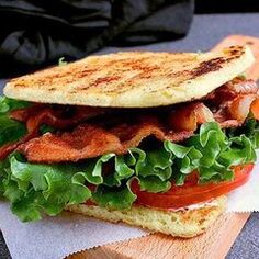 a sandwich with bacon, lettuce and tomato on it sitting on a cutting board