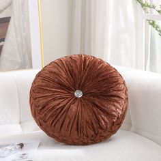 a brown round pillow sitting on top of a white couch next to a plant in a vase