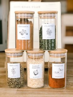 four jars filled with spices sitting on top of a wooden table