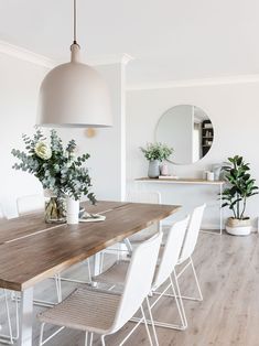 a dining room table with white chairs and potted plants