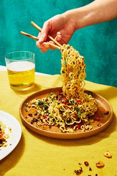 someone is eating noodles with chopsticks on a plate next to a glass of beer